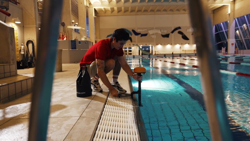 Professional from Athlee.com sets up and adjusts a lane-side camera, demonstrating the impact of Mindful Swimming's video analysis on swim coaching, highlighting the detailed and personalized approach to improving swim techniques.