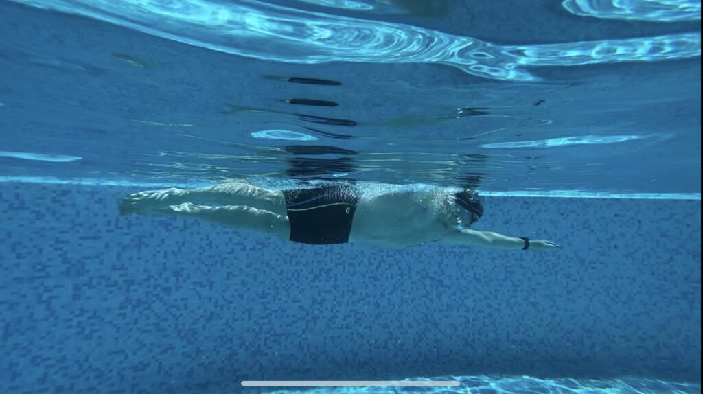 Underwater photo capturing a swimmer in black swim shorts and a black swim cap, gracefully moving through the clear pool water.