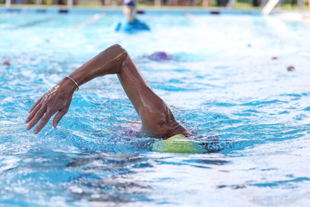 Swimmer in a pool wearing a yellow swim cap, diligently practicing laps and perfecting stroke techniques under clear blue water.