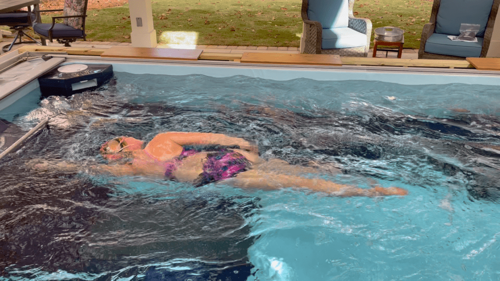 A female swimmer, dressed in a purple bathing suit, trains in an endless pool, perfecting her technique in a continuous stream of water.