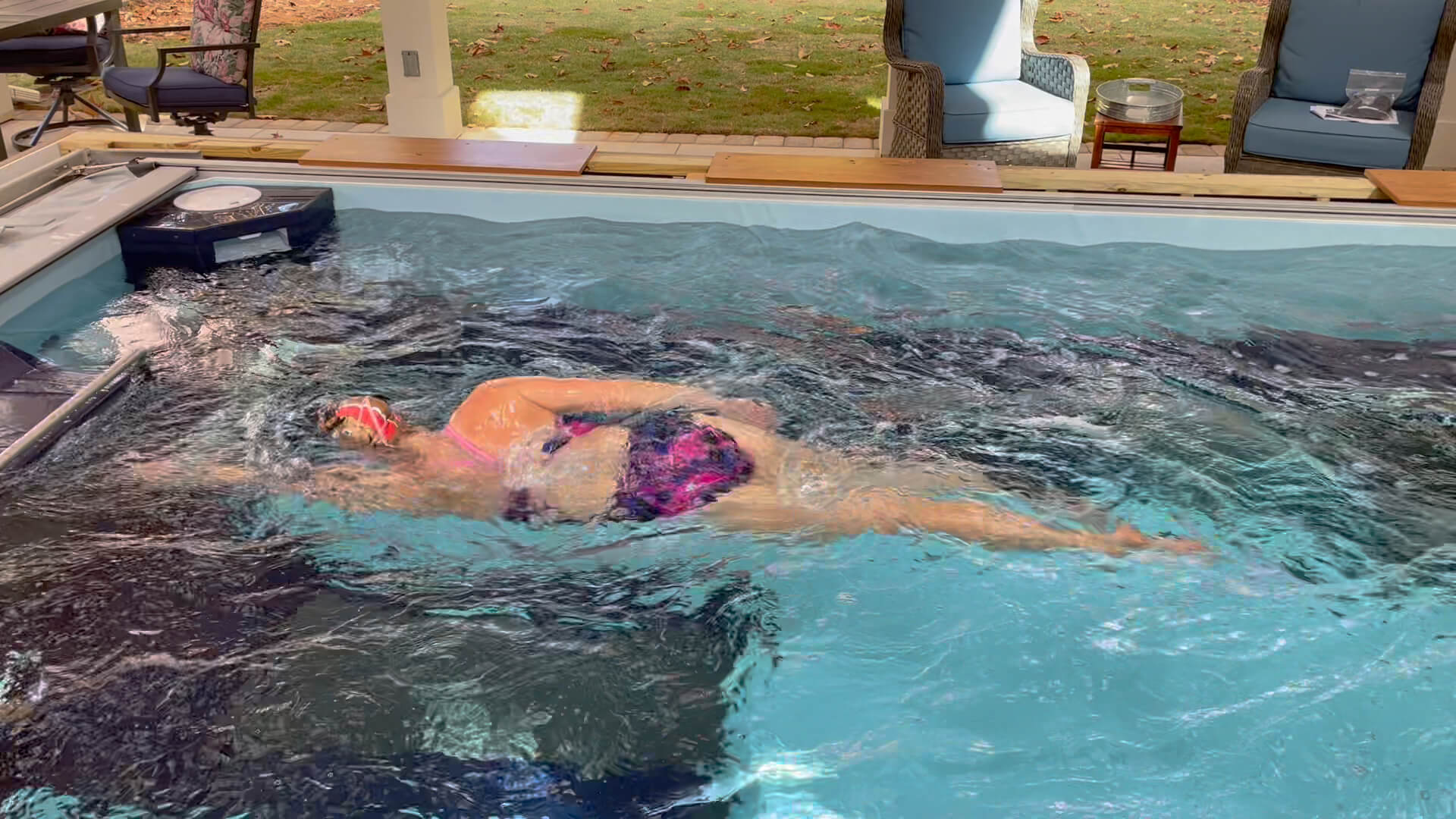 A female swimmer in a vibrant purple bathing suit harnesses her stroke in an endless pool, engaging in intense training focused on refining her swimming technique.